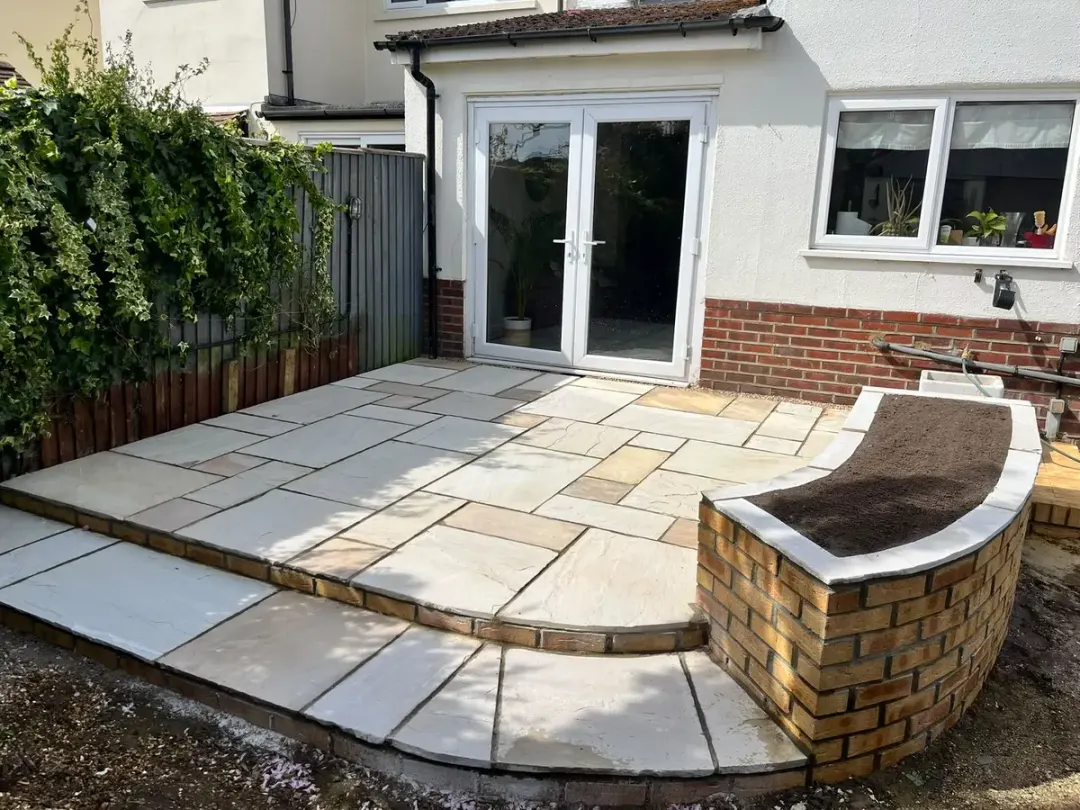 Sandstone patio with curved brick planter wall outside French doors