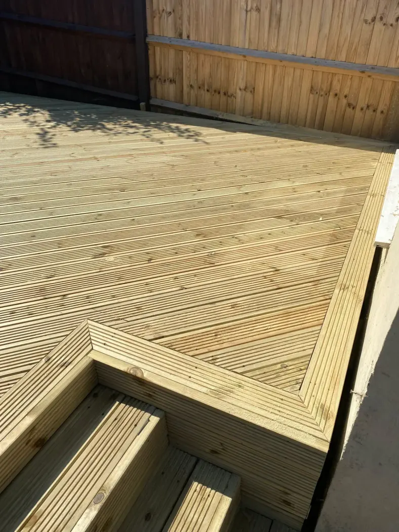 Timber decking with built-in corner steps beside a fence