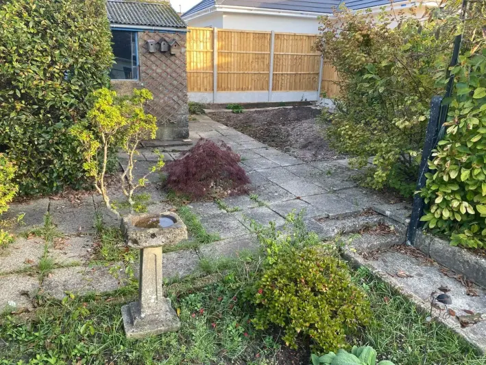 Garden before the work: cracked and uneven old paving with weeds and bare soil