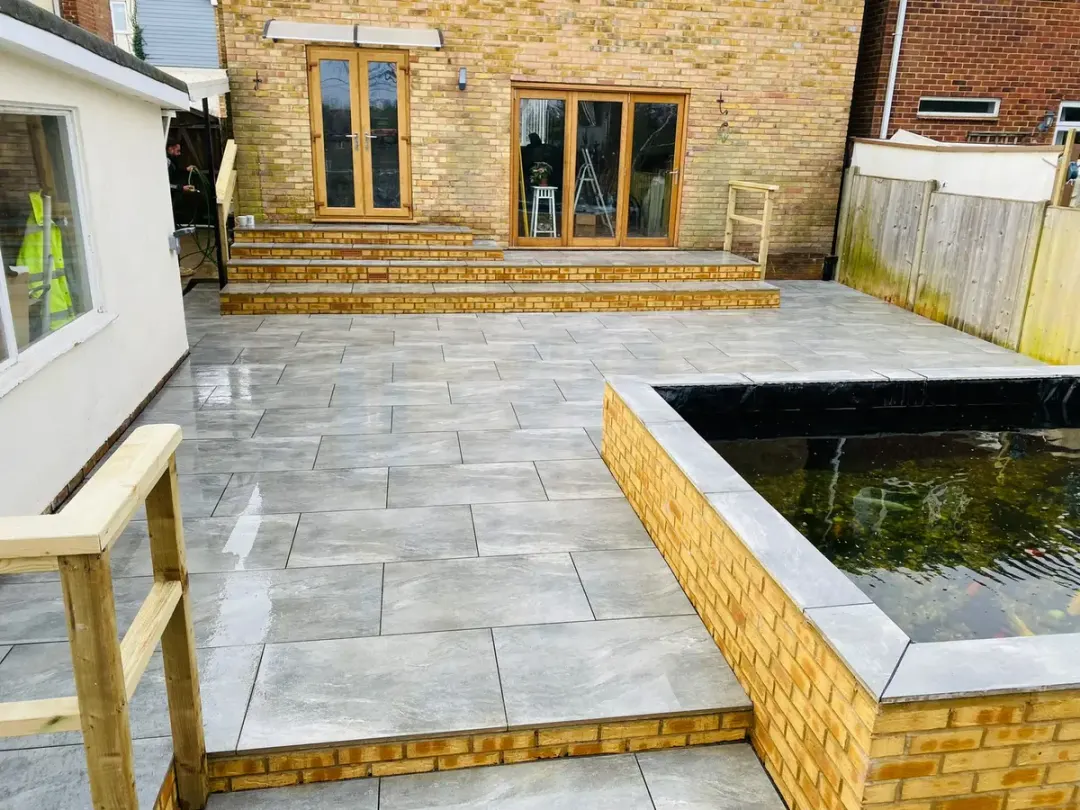 Grey porcelain patio with brick-built raised pond and wide steps to the house