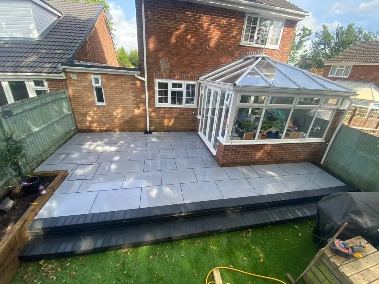 Raised grey porcelain terrace with dark step edging beside a conservatory