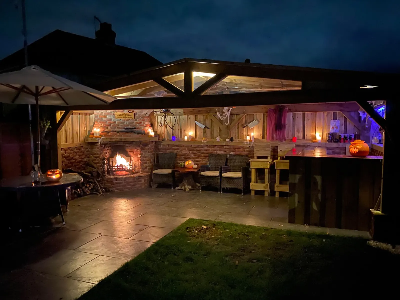 Covered timber outdoor bar with fireplace and lighting at night